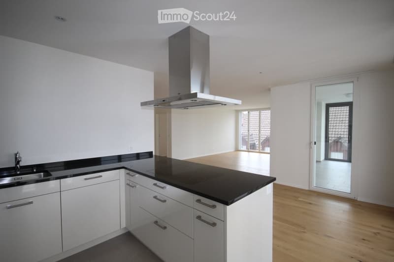 Modern kitchen with white cabinets, black countertops, a stainless steel sink, and a range hood. The floor is wooden, and there is a large window with a view of an outdoor area.