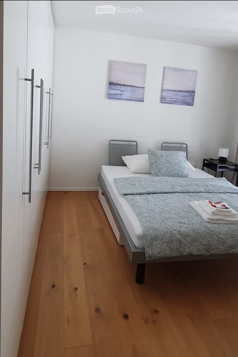 A small, neatly arranged bedroom with a single bed, nightstand, lamp, and two picture frames on the wall.