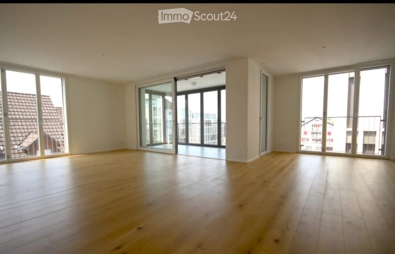 Empty room with wooden flooring, large windows, and sliding glass doors leading to a balcony.