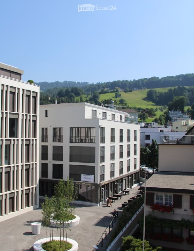 modern white building, multi story, several balconies, greenery on facade, raised ground floor, outdoor seating, green slopes in background