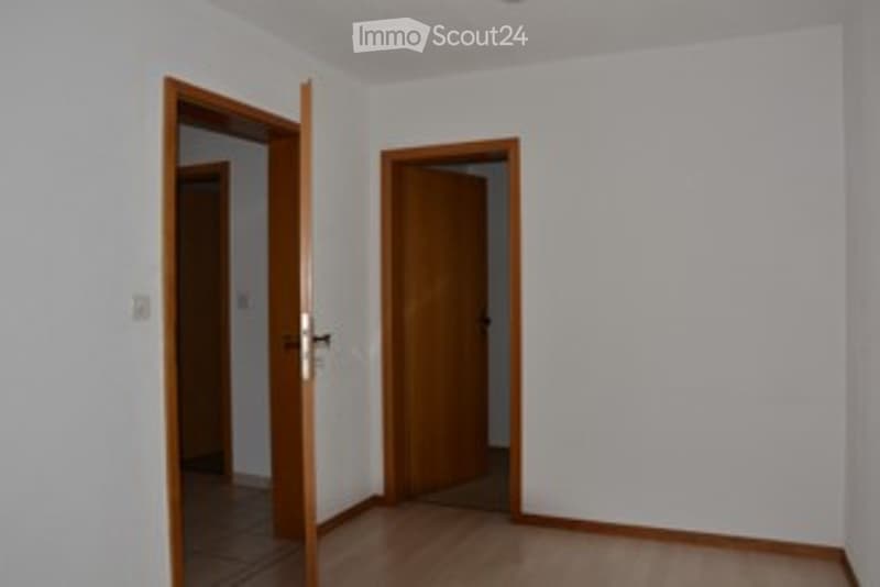 Empty room with wooden flooring, white walls, and two open wooden doors leading to adjacent spaces.