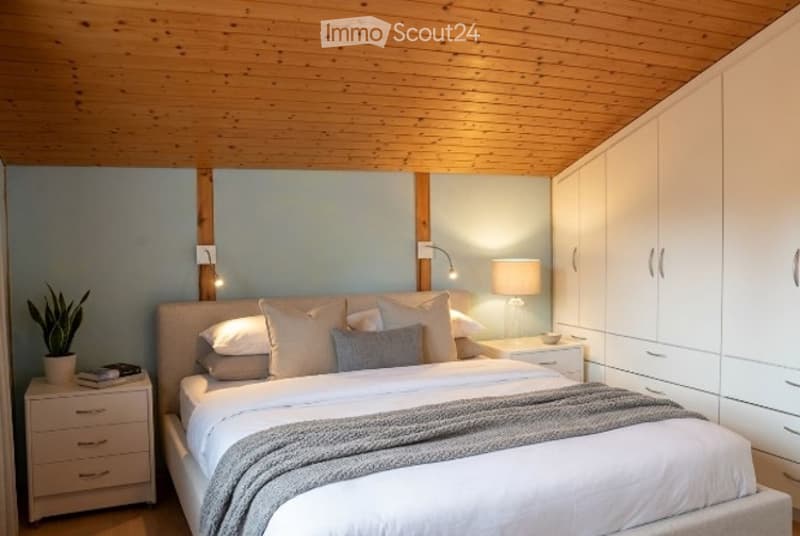 Modern bedroom with a large bed, white bedding, nightstand with lamp, potted plant, and built-in white wardrobe.