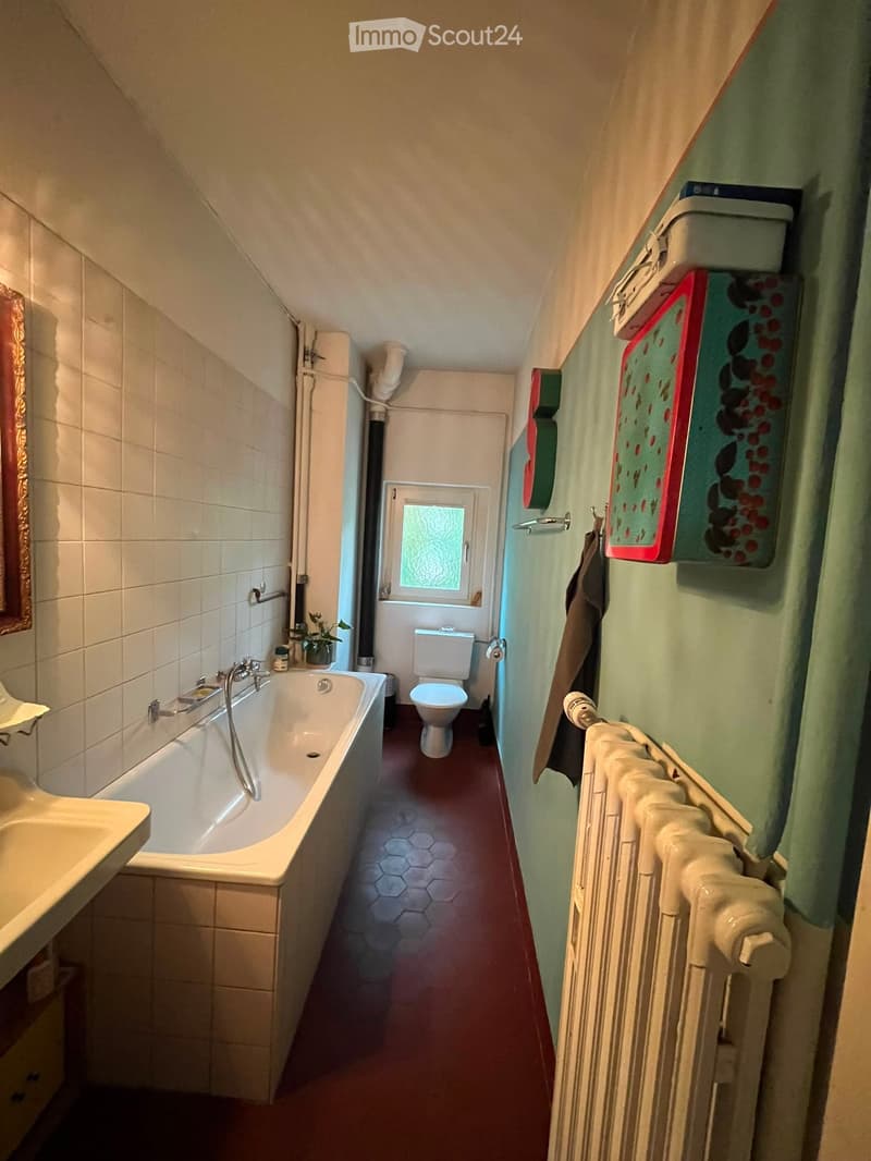 Bathroom with a bathtub, toilet, sink, radiator, towel, mirror, and a small plant on the windowsill.