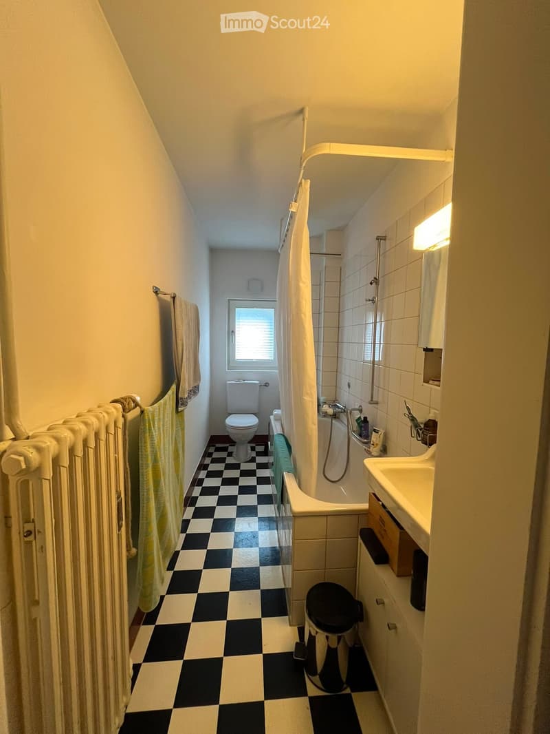 Bathroom with checkered black and white floor, white tiled walls, toilet, bathtub, sink, radiator, and towel.