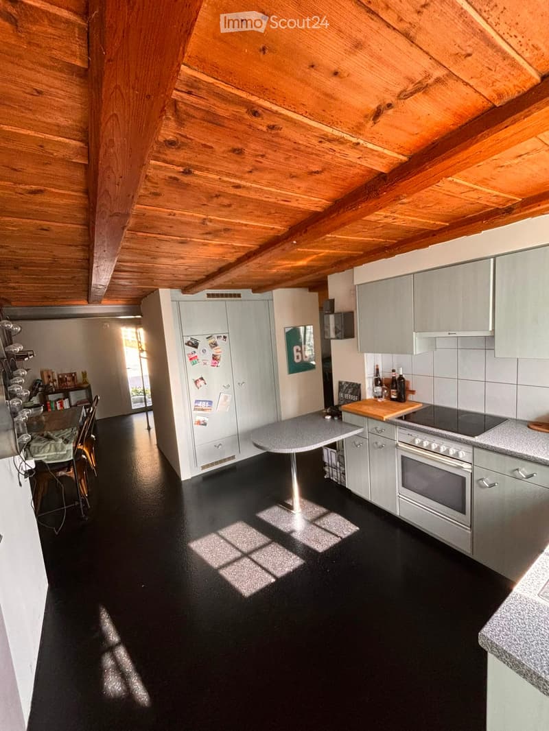 Modern kitchen with grey cabinets, black flooring, stainless steel appliances, and a small dining area with chairs and a table.