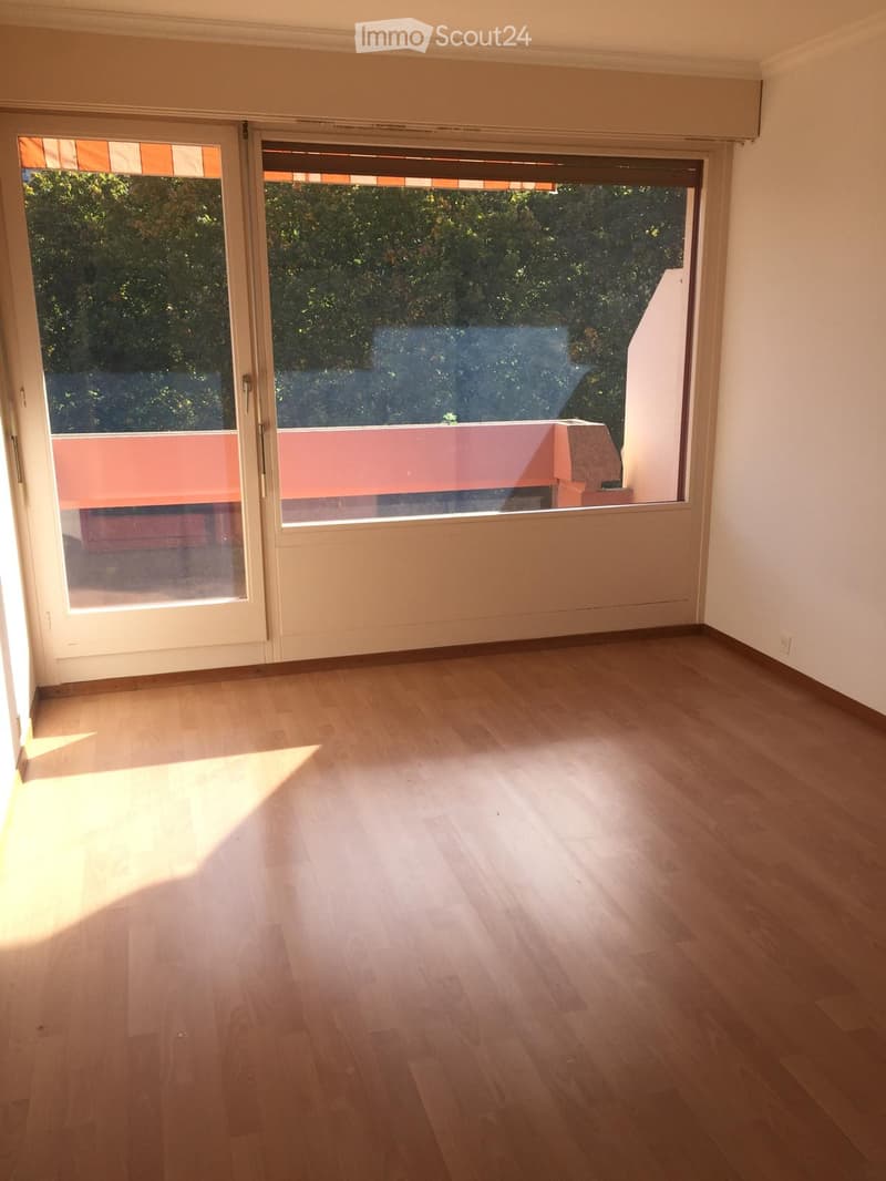 Empty room with wooden flooring, large sliding glass doors leading to a balcony, and natural light streaming in.
