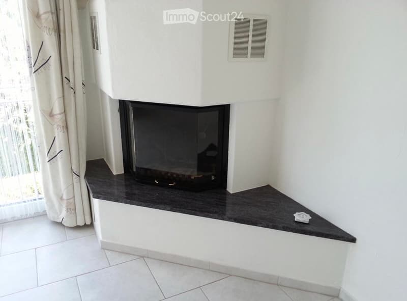 Modern fireplace with a sleek black design, white tiled floor, and a white wall with decorative vents.