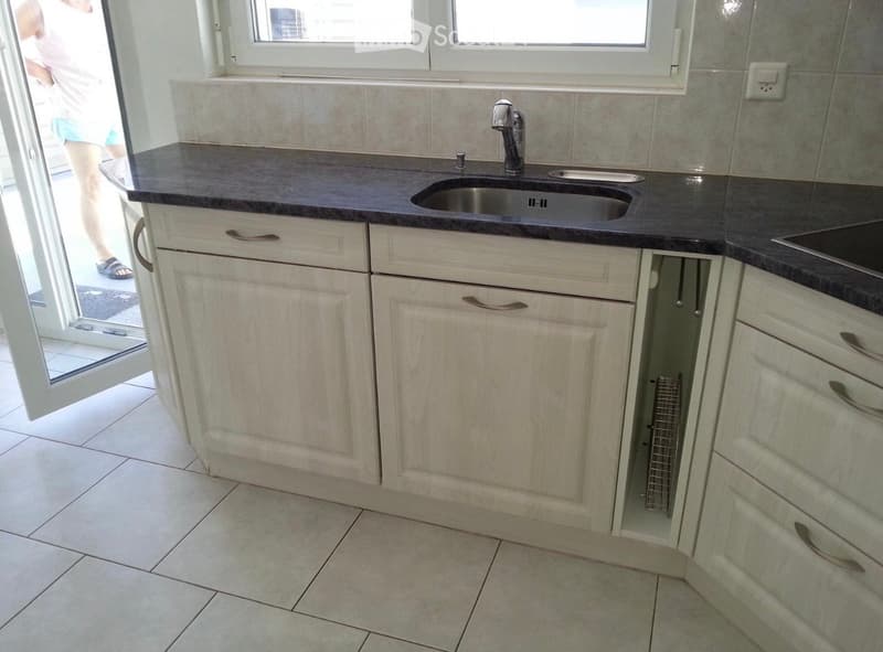 Modern kitchen with light-colored cabinets, a dark countertop, and a stainless steel sink. The space features tiled flooring and a window above the sink.