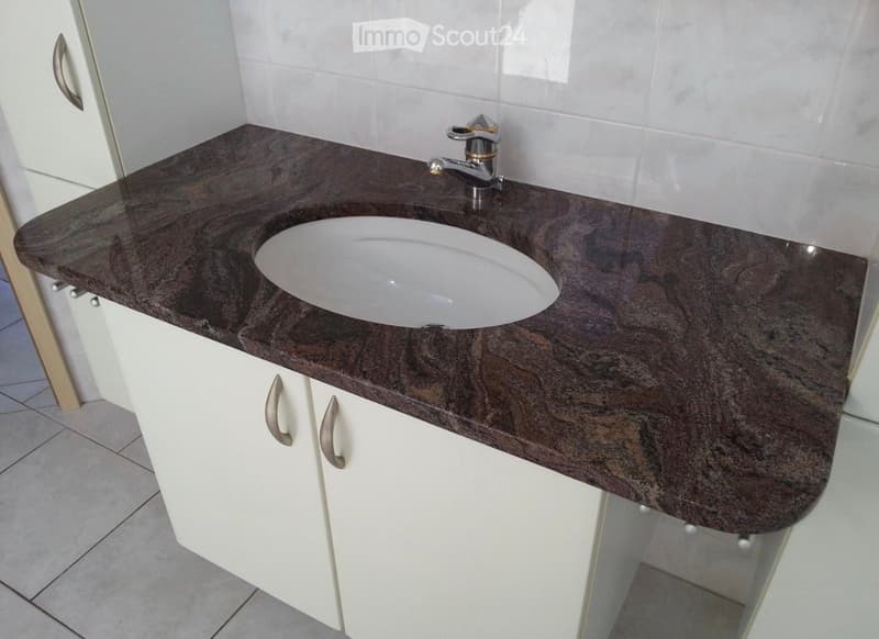 Bathroom with a dark granite countertop, white sink, chrome faucet, and white cabinets with silver handles.