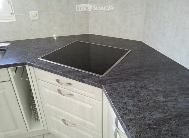 Modern kitchen with a dark grey granite countertop, white cabinets, and an induction cooktop.