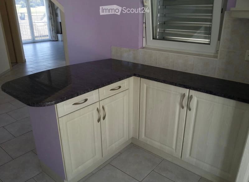 Modern kitchen with white cabinets, dark granite countertop, and tiled flooring. Features a window with blinds and an open doorway leading to a tiled patio area.