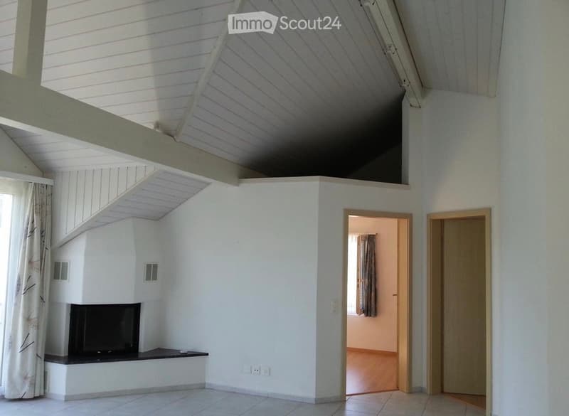 Bright living room with white walls, tiled floor, fireplace, and a large window with curtains. The room features an open staircase leading to an upper level.
