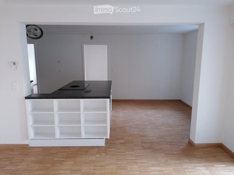 An empty room with a kitchen island and shelves, tiled floor, wooden door, white walls, and white ceiling.