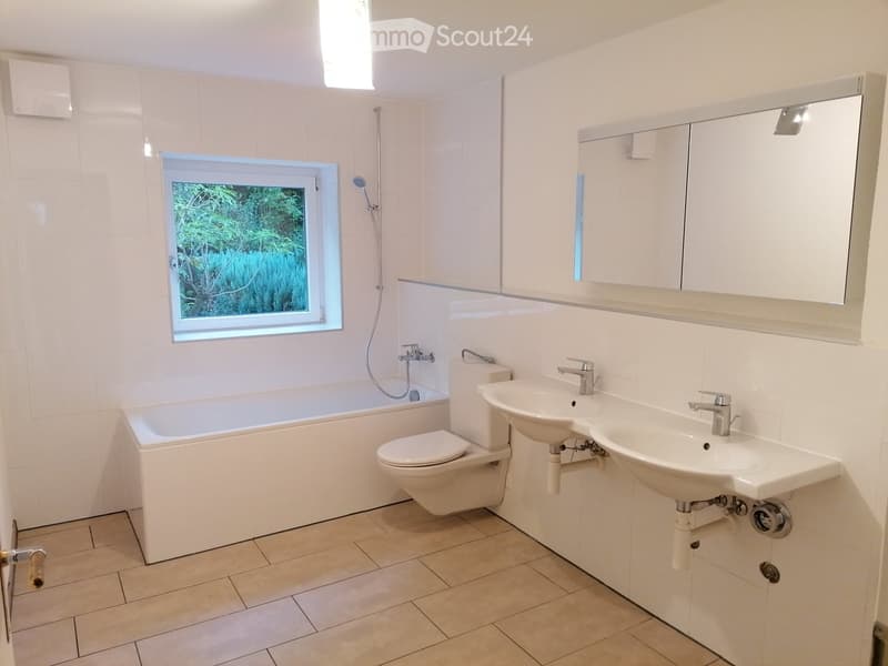 modern bathroom with white bathtub, white toilet, double vanity with sinks, overhead shower