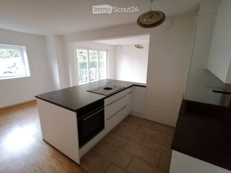 Modern minimalist kitchen with island, black granite countertop, white cabinets, stainless steel oven, integrated sink, natural wooden flooring, two windows, balcony with railings
