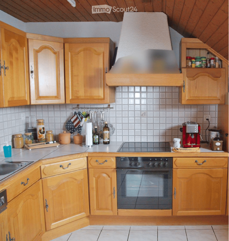 A cozy kitchen with wooden cabinets, a central island, and various appliances including an oven, stove, and coffee maker. The space features tiled walls and a range hood above the stove.