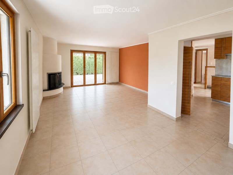 Empty living space with tiled floor, fireplace, large sliding glass doors leading to outdoor area, and adjacent kitchen area with cabinets.