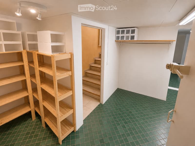 Empty room with green tiled floor, white walls, wooden shelving units, and a small staircase leading to another area.