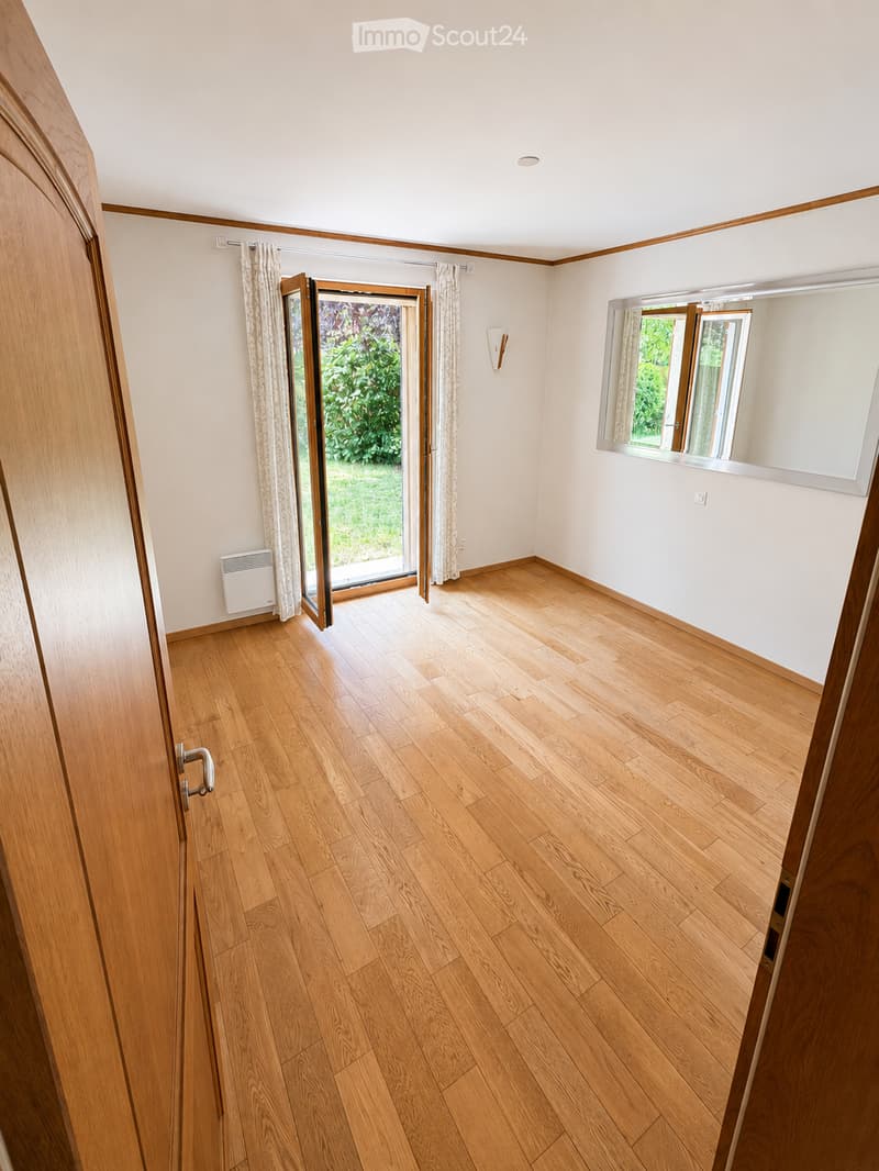 Empty room with wooden flooring, white walls, large sliding glass door leading to outdoor area, and a mirror on the wall.