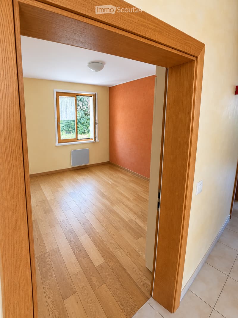 Empty room with wooden flooring, light-colored walls, a window with white frame, and a radiator. The room is unfurnished and has a simple, clean design.