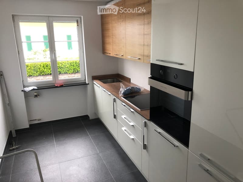 Modern kitchen with white cabinets, wooden countertop, built-in oven, and a window overlooking a green area.