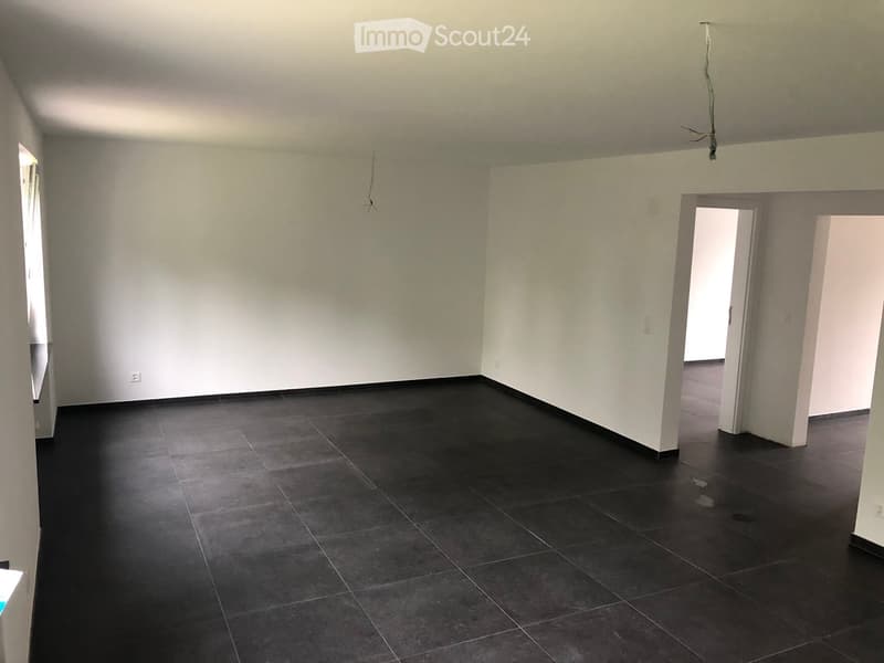 Empty room with dark tiled floor and white walls, featuring two open doorways leading to other spaces.