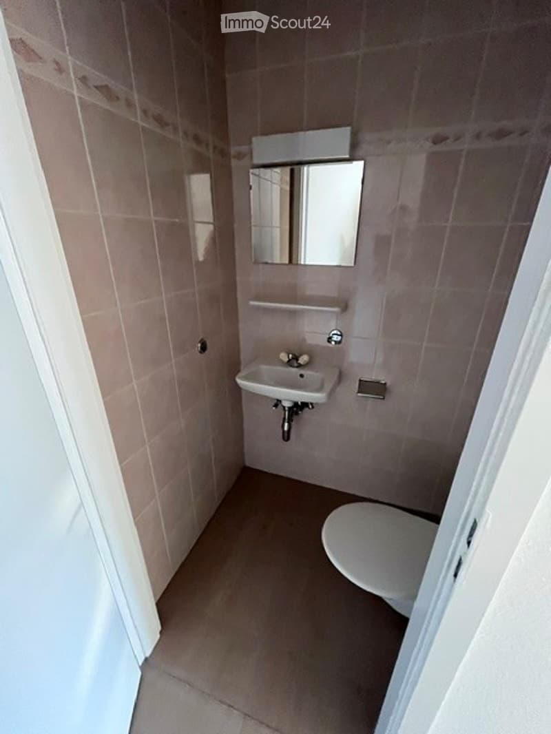 Small bathroom with beige tiles, a white sink, a mirror above it, and a toilet. Includes a towel rack and a faucet.