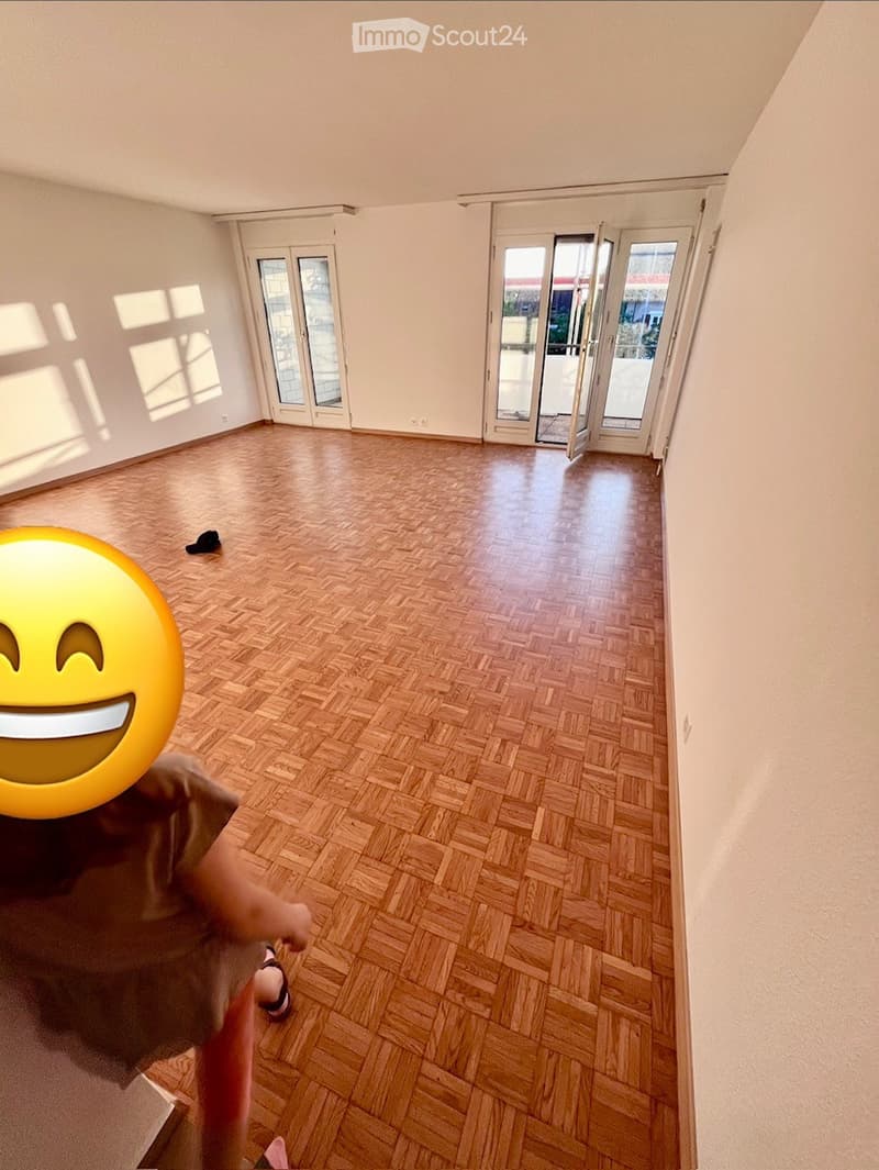 Empty room with wooden herringbone flooring, white walls, and large glass doors leading to a balcony.