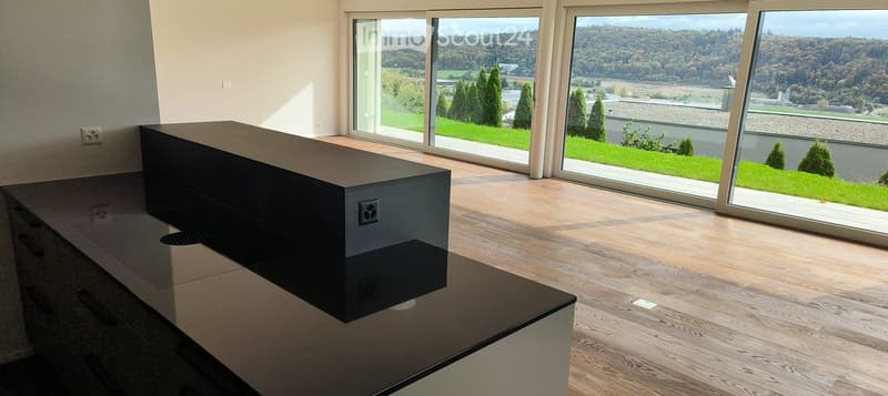 Modern living room with large windows offering a scenic view, featuring a sleek black table and wooden flooring.