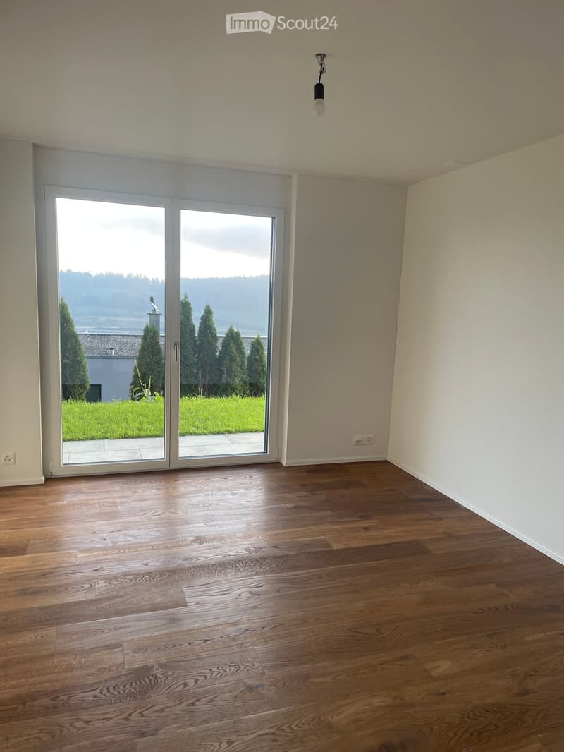 Empty room with wooden flooring, large sliding glass doors leading to a grassy outdoor area, and white walls.