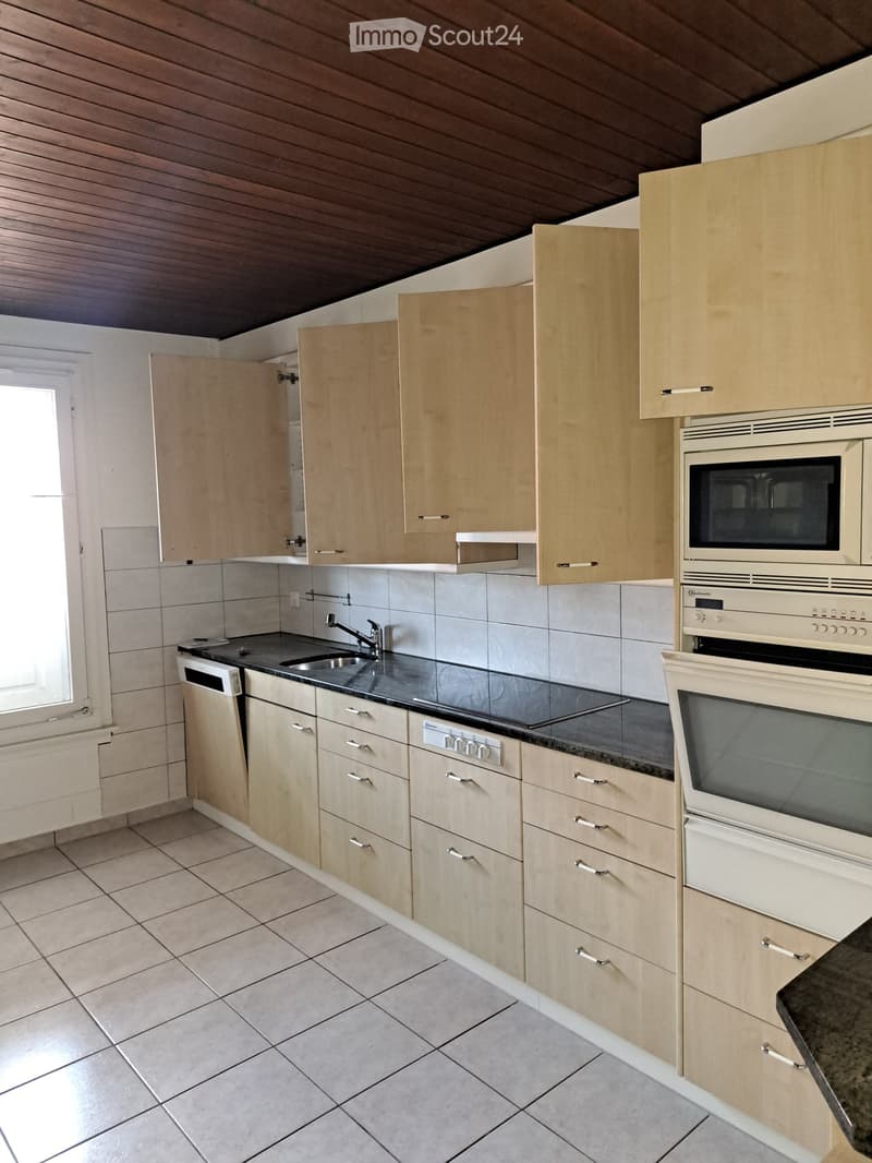 Modern kitchen with light wood cabinets, stainless steel sink, microwave, oven, and dishwasher.