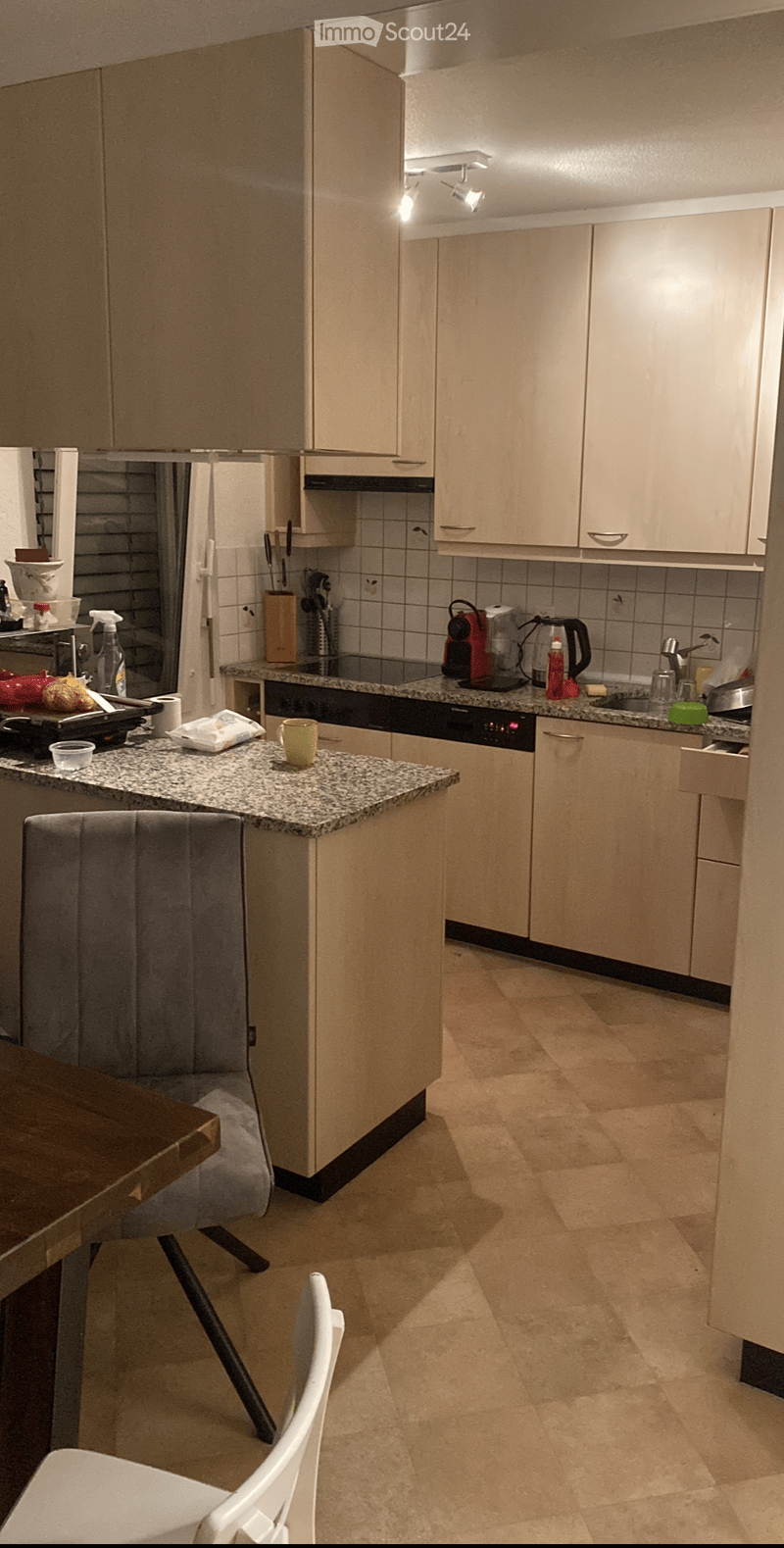 Modern kitchen with light-colored cabinets, granite countertops, and various appliances including a coffee maker, oven, and dishwasher. There is a small dining area with a table and chairs.