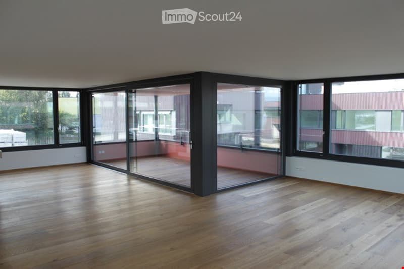 Empty room with wooden flooring, large windows, and a sliding glass door leading to a balcony.