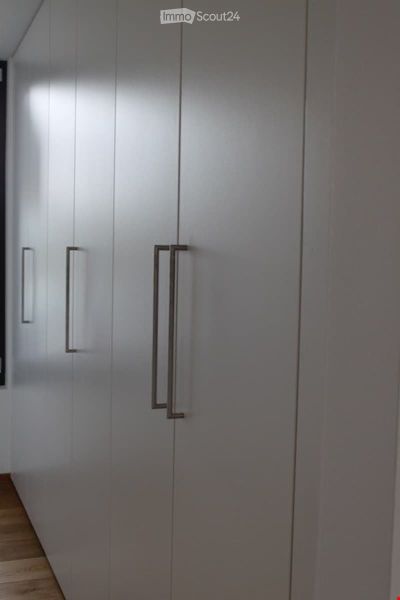 A modern hallway with sleek, grey built-in wardrobes featuring minimalist handles and a polished wooden floor.