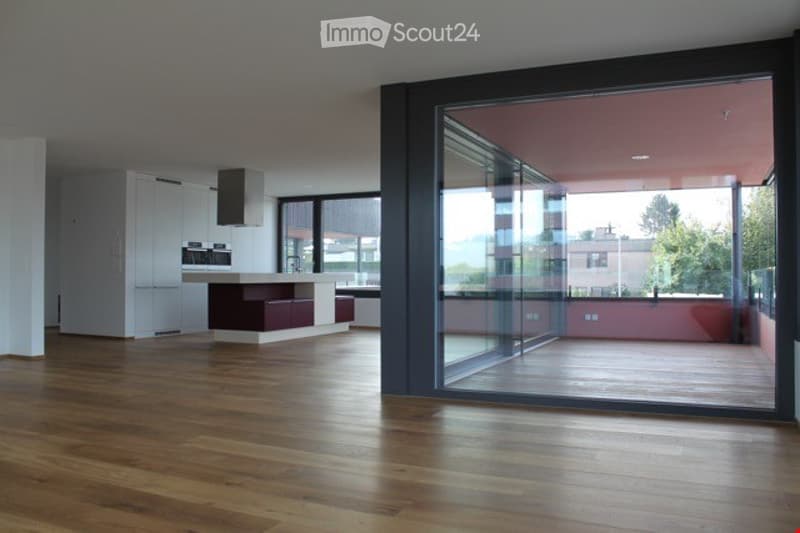 Modern, open-plan kitchen and living area with wooden flooring, large glass sliding doors leading to a balcony, built-in cabinets, and a central kitchen island.
