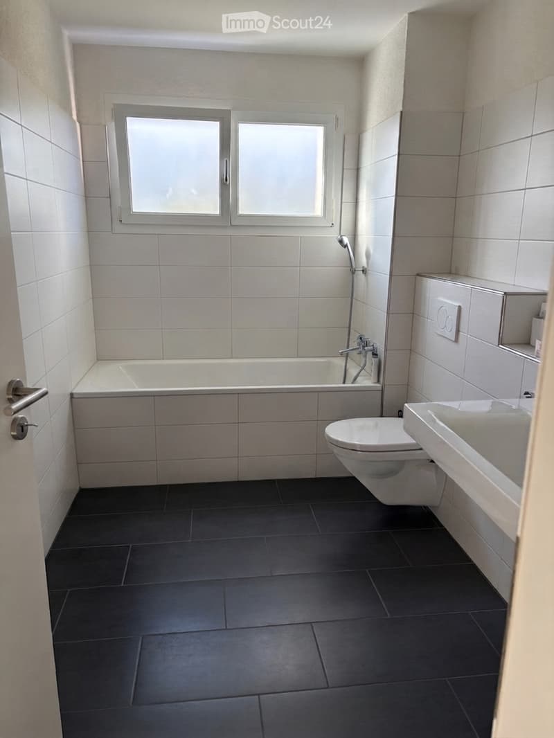 Modern bathroom with white tiled walls, black tiled floor, bathtub, toilet, sink, and showerhead.