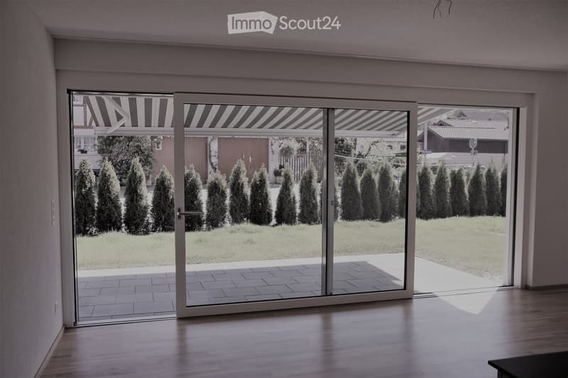 Bright hallway with large sliding glass doors leading to a well-maintained garden with neatly trimmed coniferous trees and a paved patio.