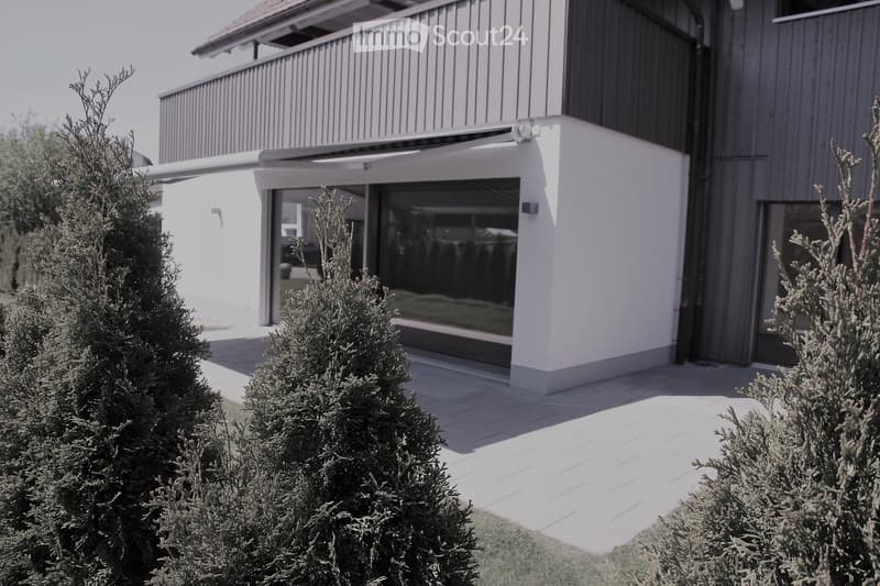 Modern two-story house with white and grey exterior, large windows, and a covered balcony area.