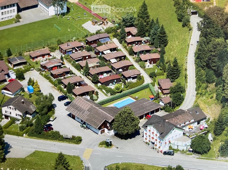 Aerial view of a residential area with multiple houses, a swimming pool, and surrounding greenery.