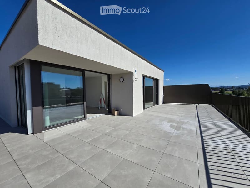 Modern balcony with large glass doors, tiled floor, and a view of the surrounding area.