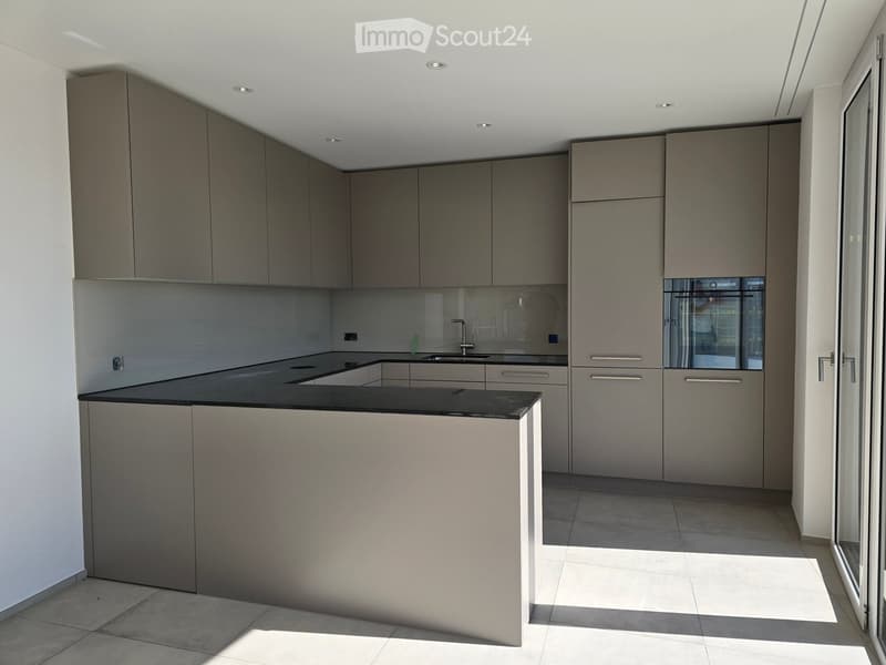 Modern kitchen with grey cabinets, black countertop, and built-in sink. Features sleek design with integrated storage and a large window providing natural light.