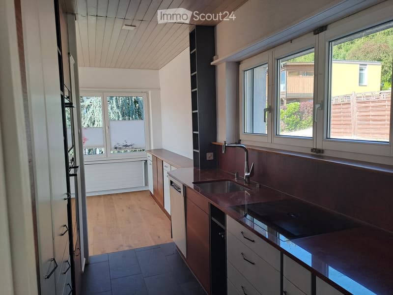 Modern kitchen with wooden cabinets, stainless steel sink, and countertop, large windows providing natural light.