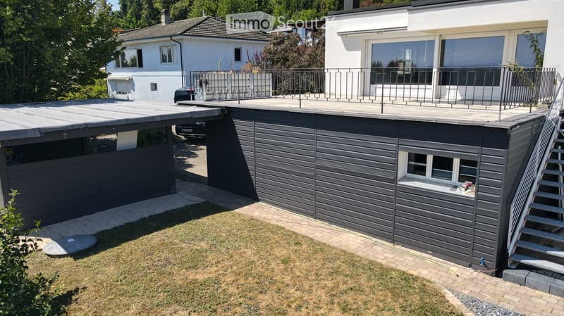 Modern two-story house with a flat roof terrace, garage, and balcony overlooking the garden.