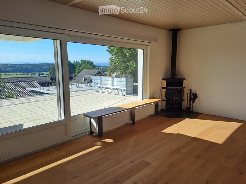 Bright living space with wooden flooring, large glass doors opening to a balcony, a bench, and a fireplace.