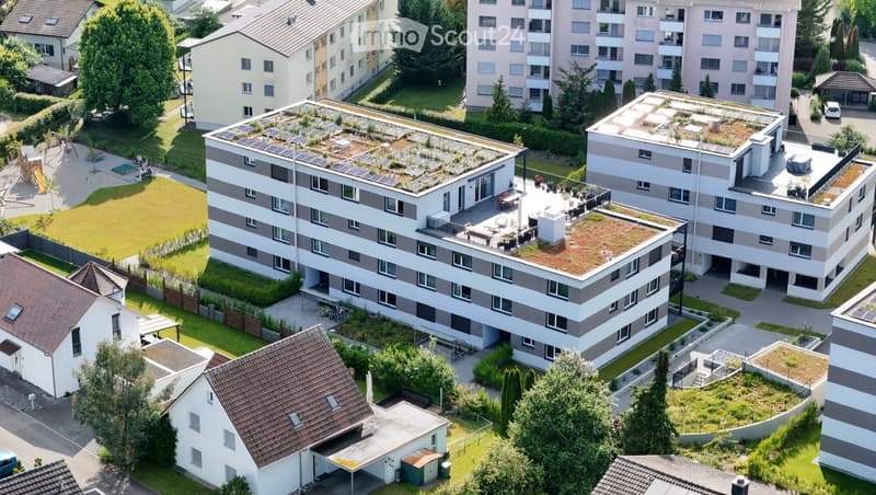 Aerial view of a residential complex with multiple apartment buildings, green roofs, and surrounding greenery.