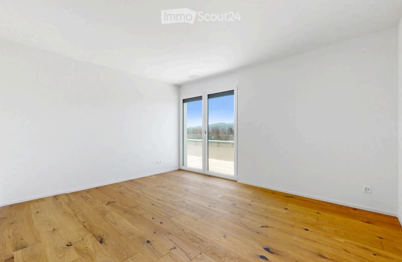 Empty room with light wooden flooring and white walls, featuring a large glass sliding door leading to a balcony.