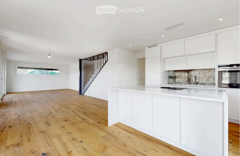 Modern kitchen with white cabinets, a central island, and a stove. The floor is made of light wooden planks, and there is a staircase visible in the background.