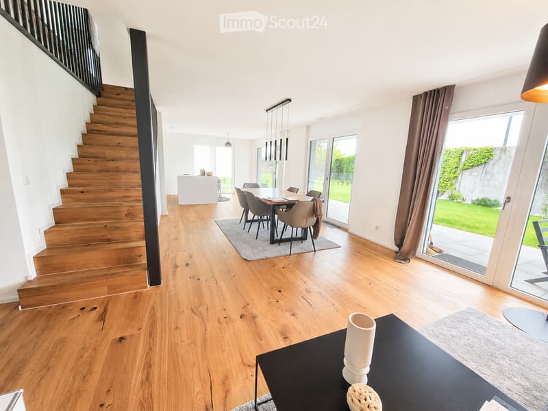 Open-plan living and dining area with wooden flooring, staircase, dining table with chairs, and a coffee table with decorative items.