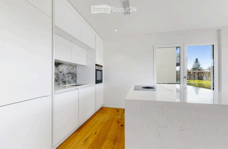 Modern kitchen with white cabinets, wooden flooring, and a large island countertop. Features a sink, faucet, and built-in oven.