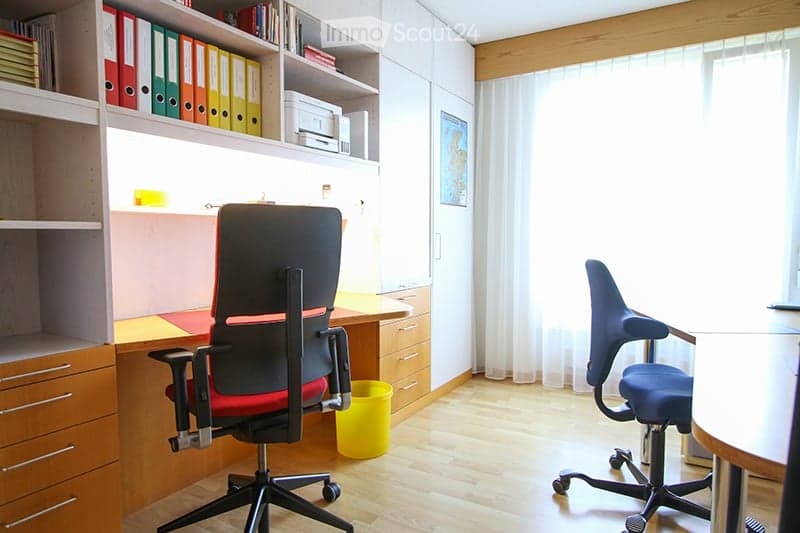 A modern office space with two ergonomic chairs, a desk, a cabinet, and shelves filled with binders and books.